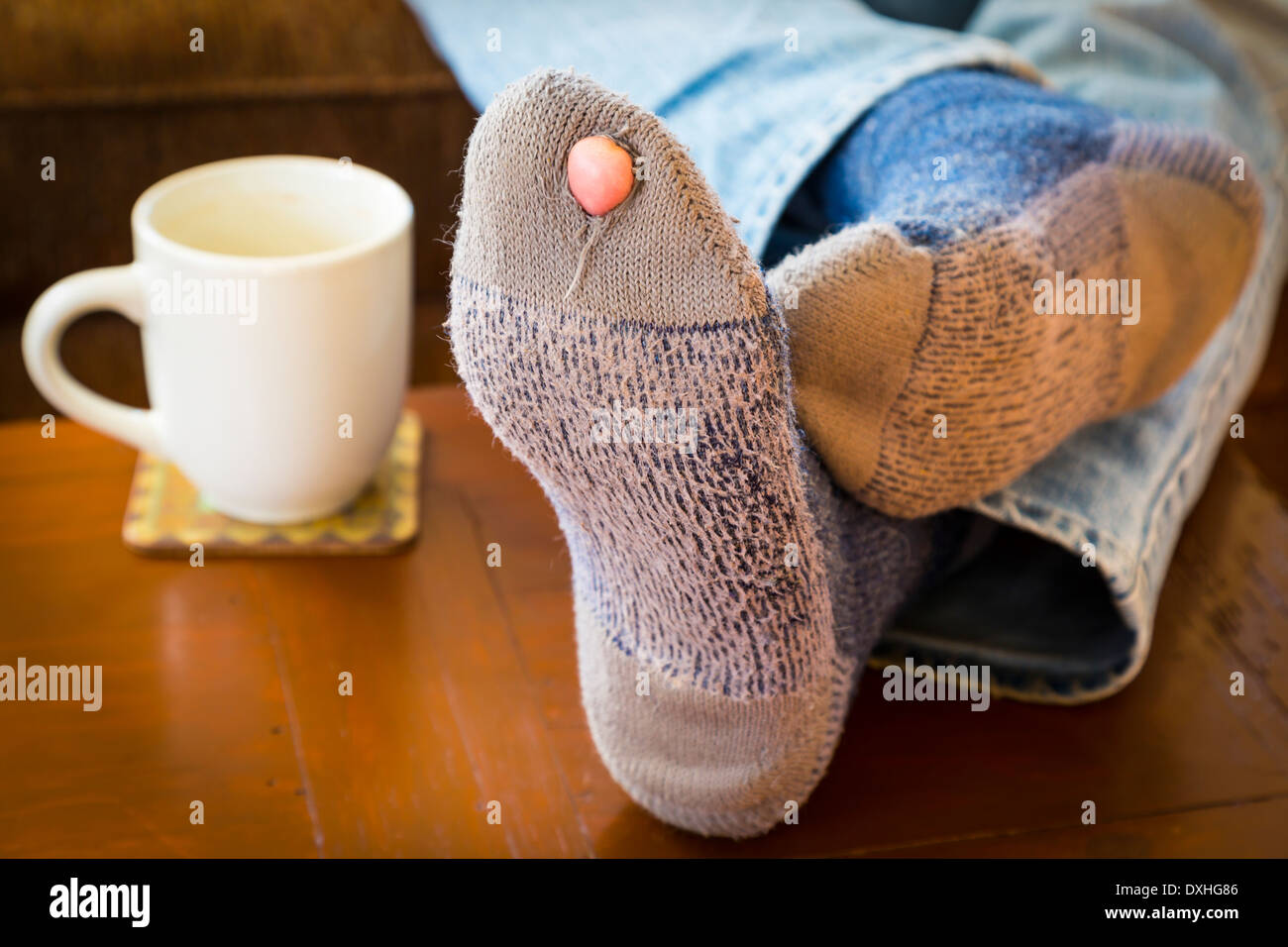 Piedi puntellato su un tavolino con una coppia di usurati calze con un foro e un piede fuori di essi. Foto Stock