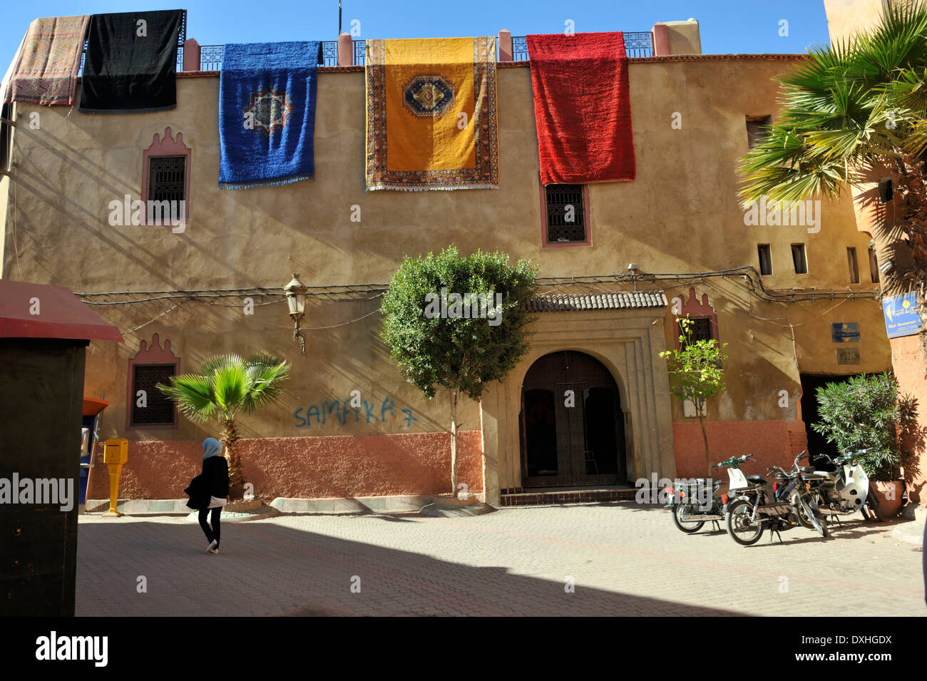 I tappeti appesi sopra la parete a livello del tetto con scena di strada al di sotto, Marrakech, Marocco Foto Stock