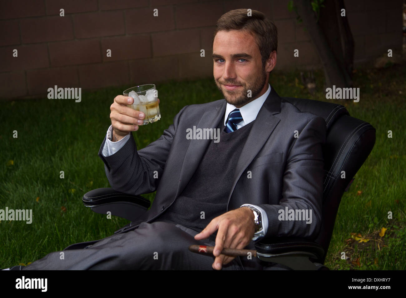 Uomo d'affari al di fuori in sedia per ufficio di bere whisky Foto Stock
