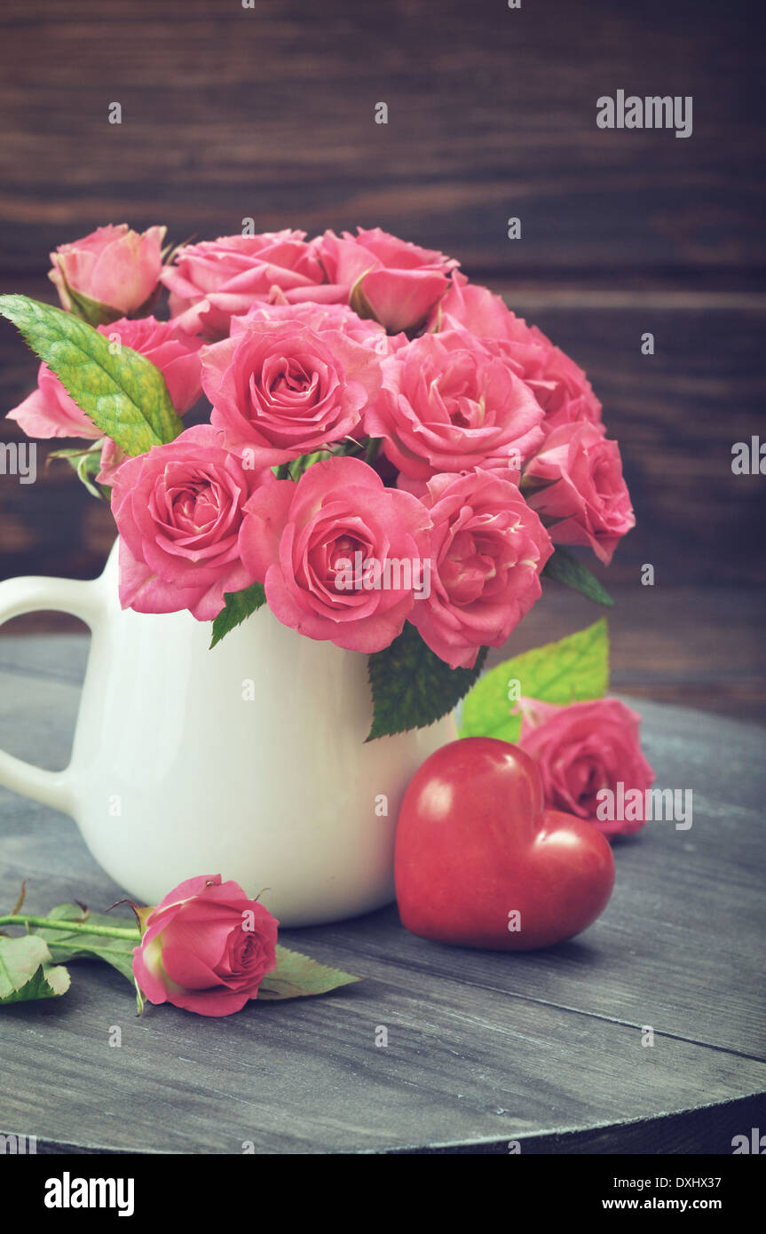 Bouquet di rose rosa in vaso con cuore di pietra su sfondo di legno Foto Stock