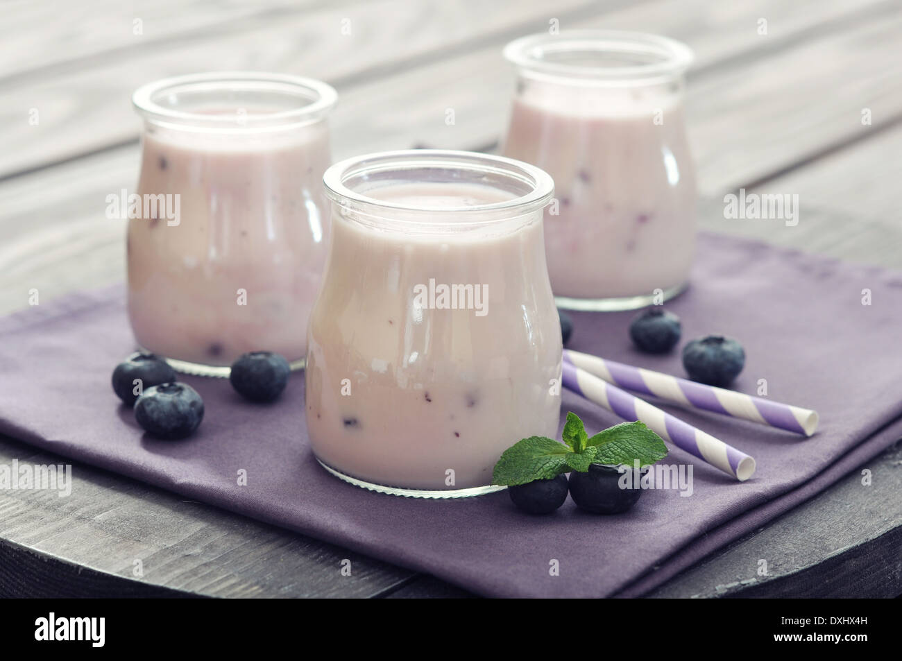 Yogurt con maturi ai mirtilli freschi in vasi su sfondo di legno Foto Stock