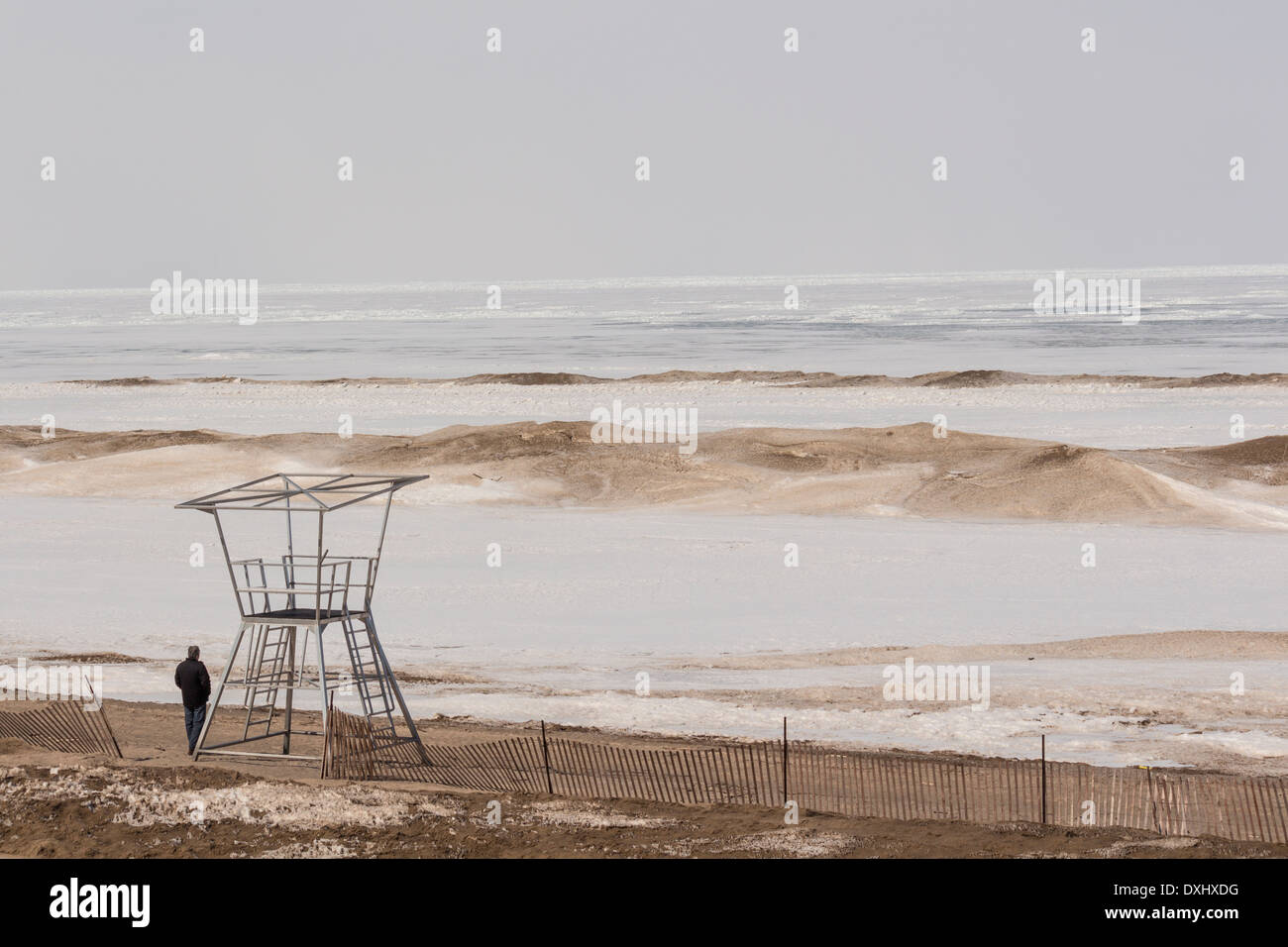Uomo in piedi accanto a vuoto di vita guard stare sulla spiaggia di Grand Bend, Ontario sul Lago Huron, che è completamente congelato. Foto Stock