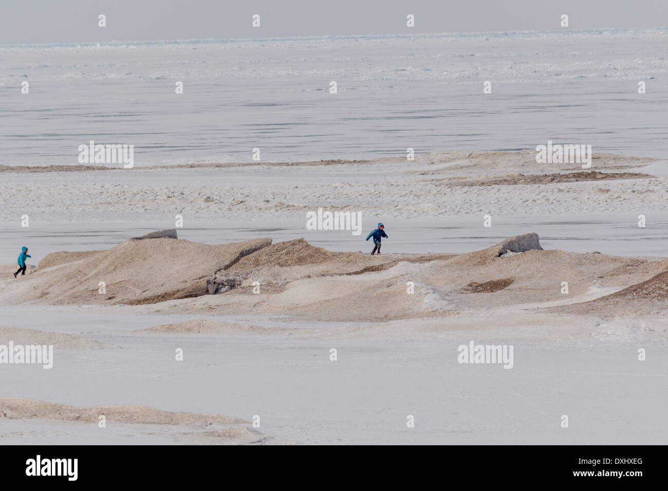 Chldren correre e giocare sulla sabbia grandi derive di neve su un completamente congelato Lago Huron in Grand Bend, Ontario Foto Stock