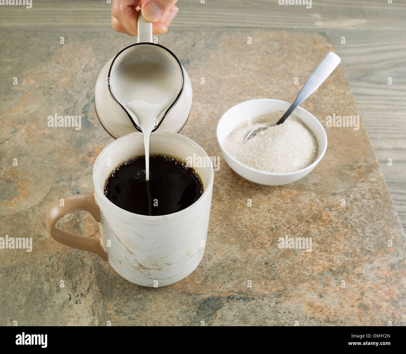 Fotografia del lato femmina versando la panna in una tazza di caffè nero con pietra e legno invecchiato sotto Foto Stock