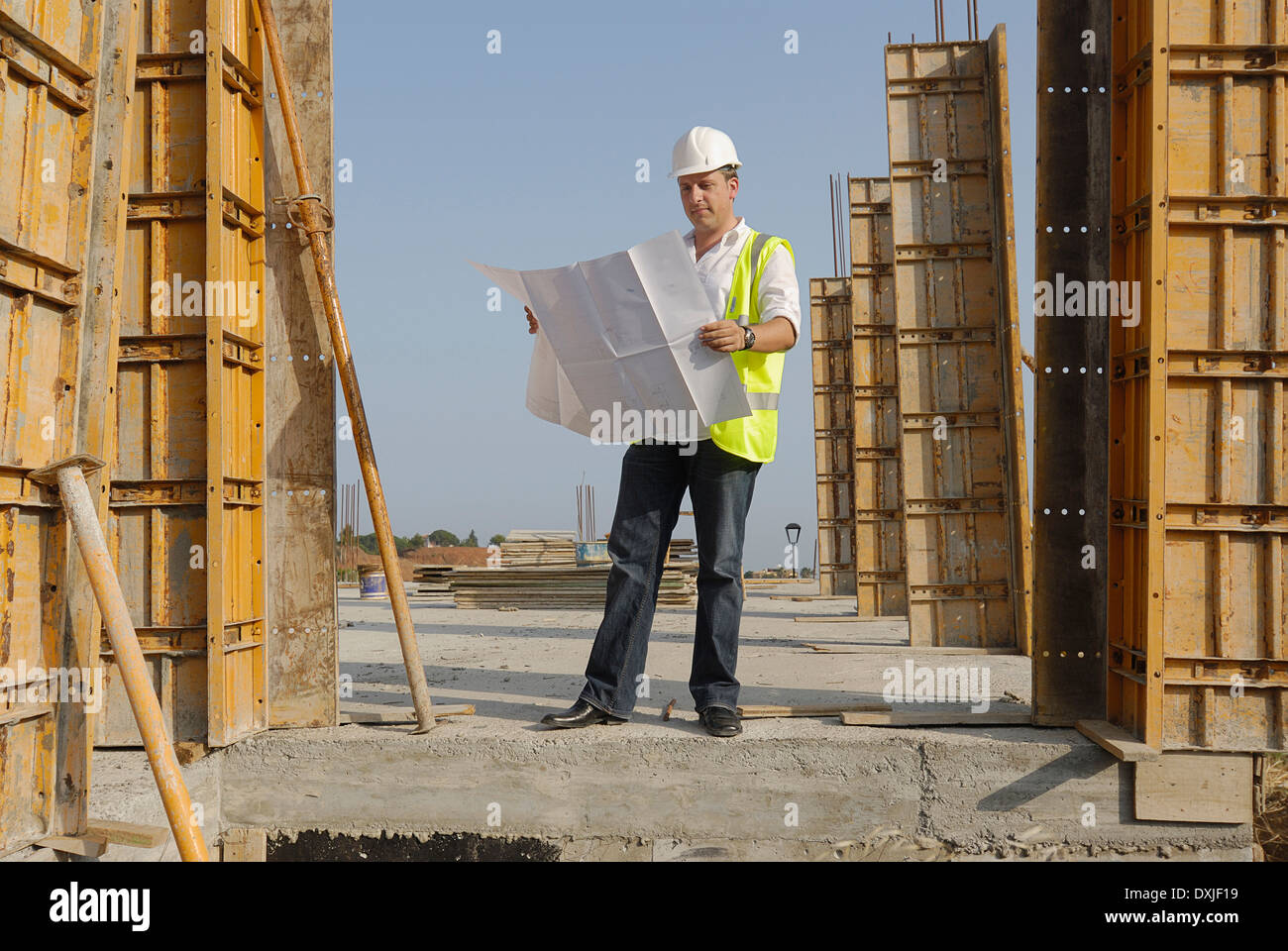 Ingegnere maschio indossare elmetto guardando i piani sul sito di costruzione Foto Stock
