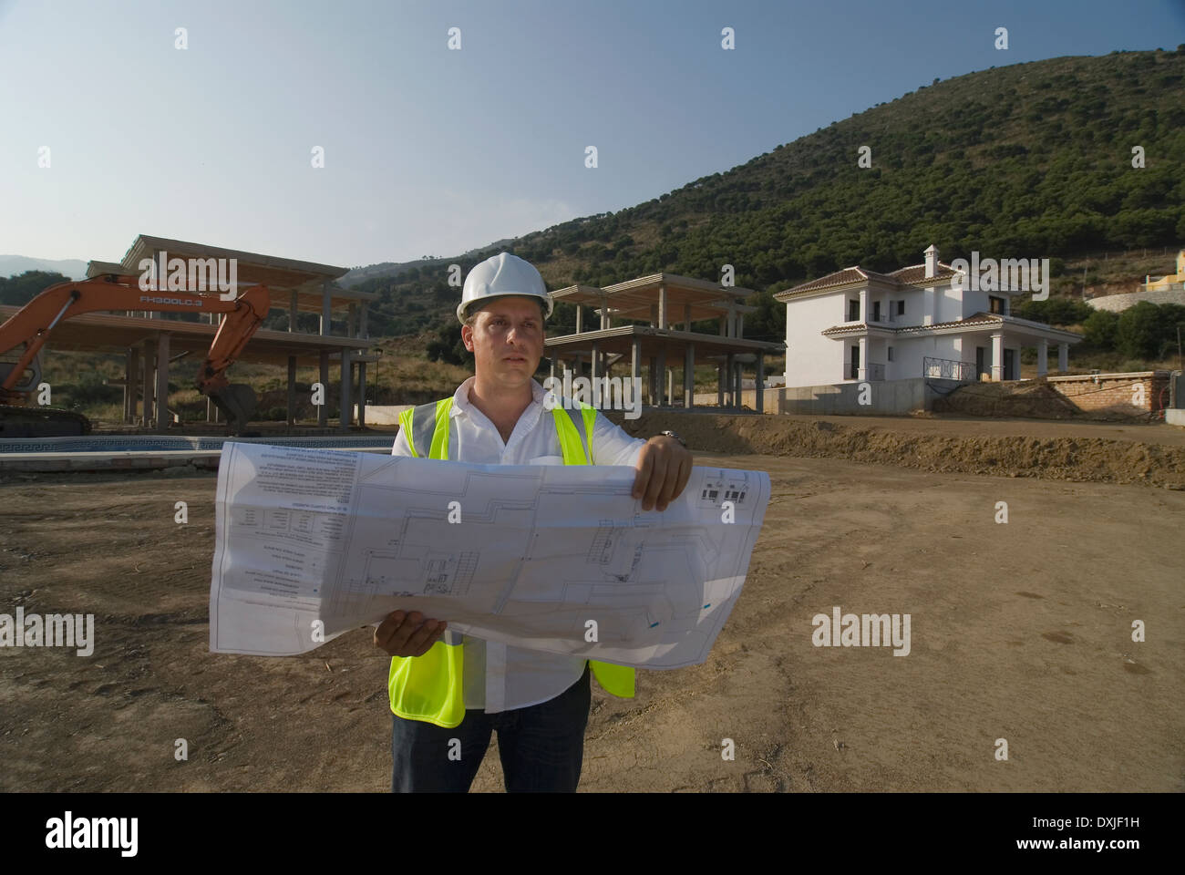 Ingegnere maschio indossare elmetto guardando i piani sul sito di costruzione Foto Stock