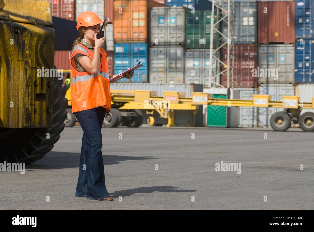 Donna che indossa elmetto utilizzando un walkie-talkie al terminale per container Foto Stock