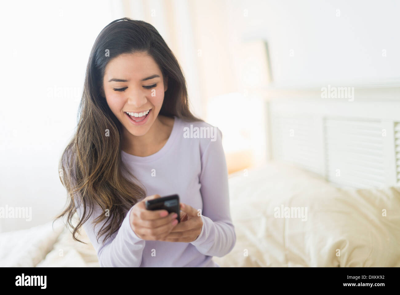 Felice donna Ispanica per la messaggistica di testo nel letto Foto Stock