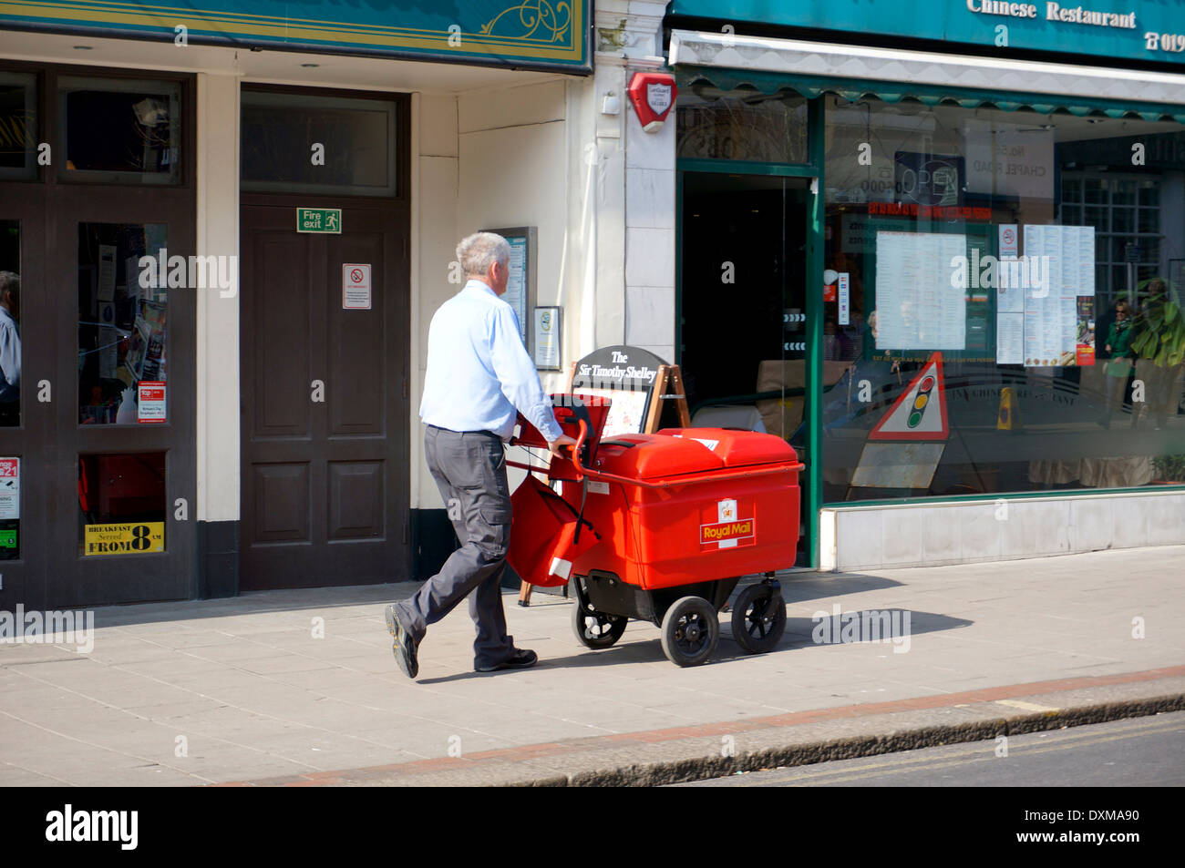 Postino sulla sua round consegnare le lettere e i pacchi utilizzando un "Alta Capacità" carrello (sostituzione della vecchia bicicletta) Foto Stock