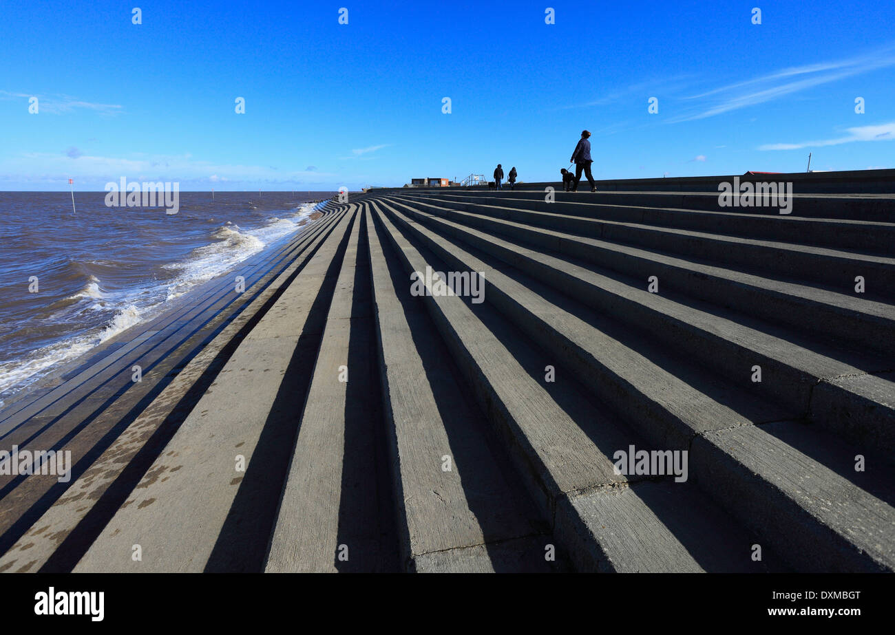 Walkers lungo la parte superiore della parete del mare ad alta marea a Heacham sulla costa di Norfolk. Foto Stock