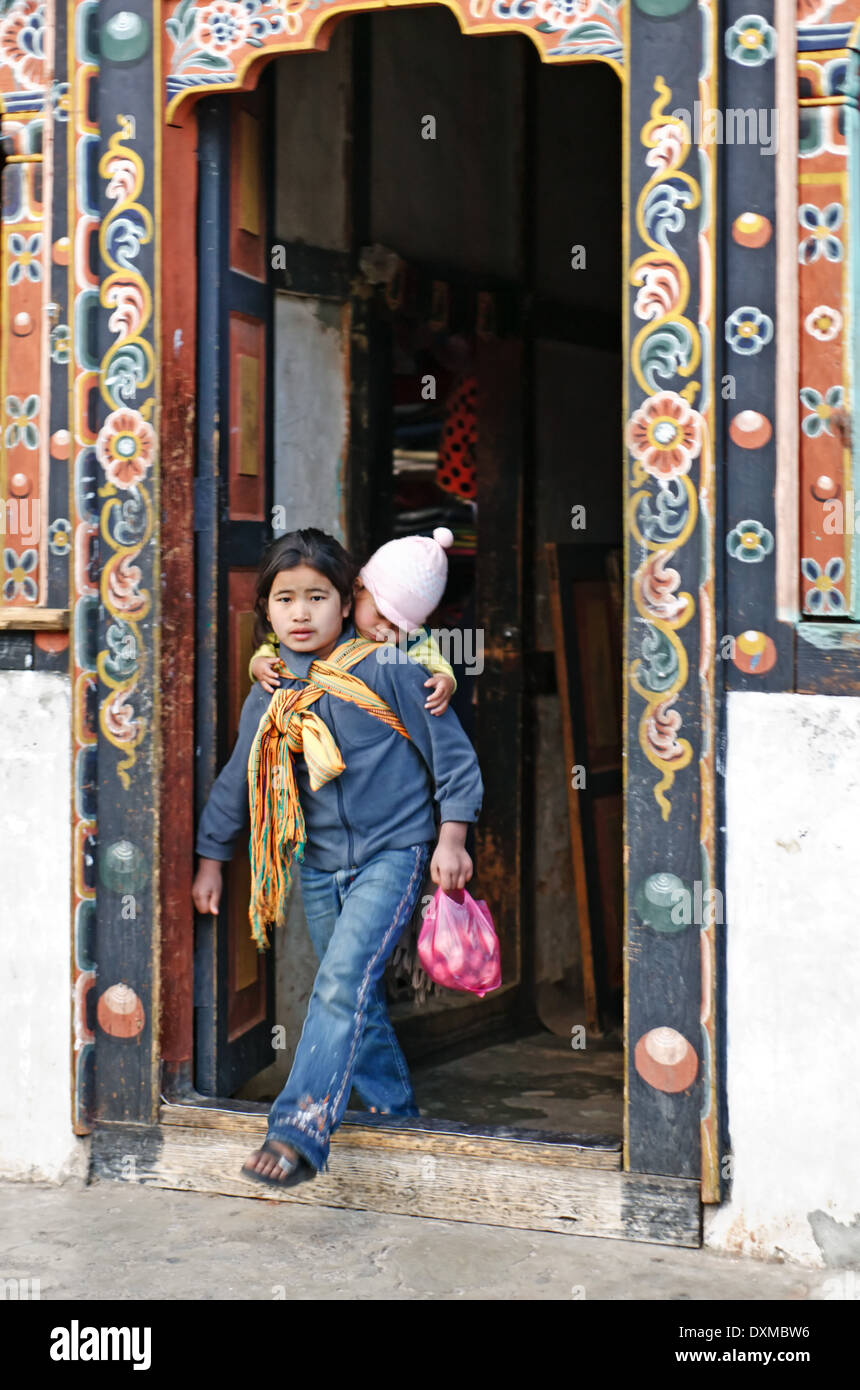 Giovane donna che porta un bambino in una imbragatura posteriore esce da un portale colorato a paro, Bhutan Foto Stock