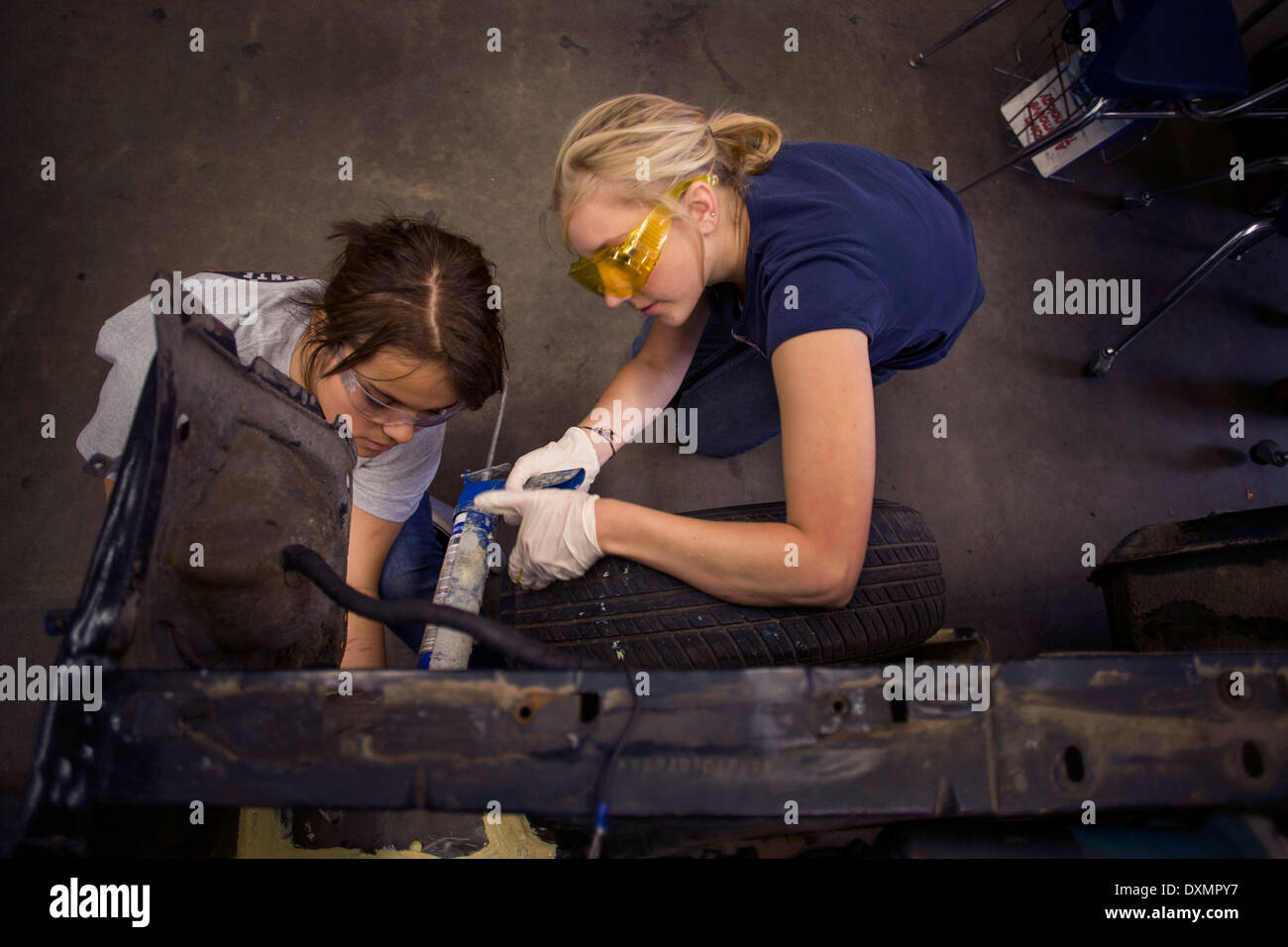 Indossare occhiali di sicurezza due ragazze adolescenti a lavorare insieme su un auto in auto shop classe in San Clemente, CA. Foto Stock