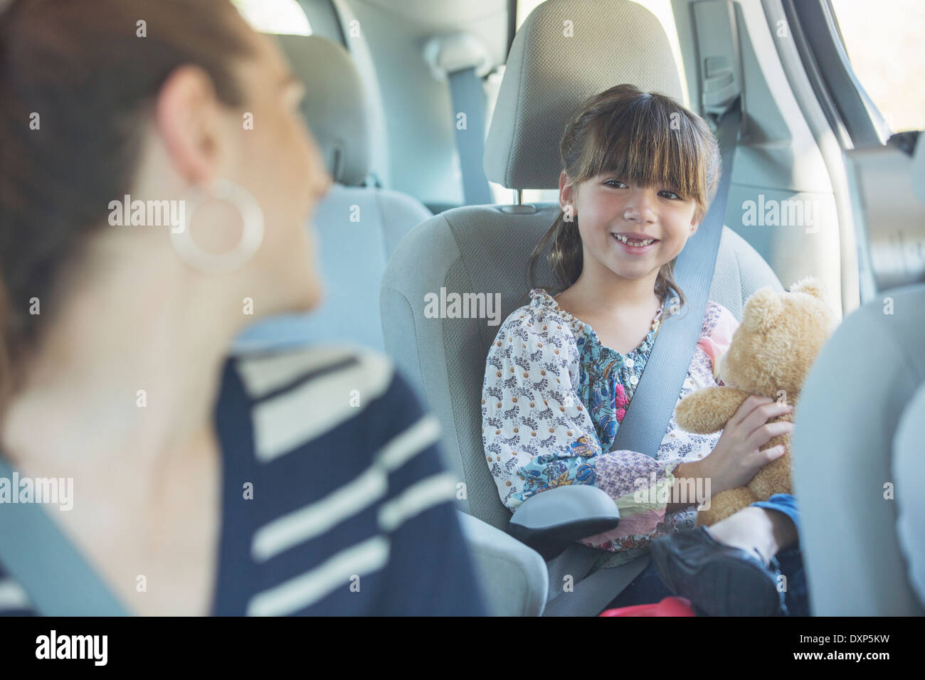 Madre di tornitura e sorridente a nostra figlia nel sedile posteriore della macchina Foto Stock
