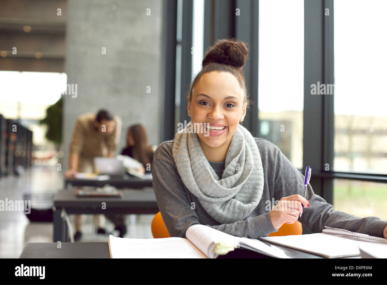 Felice giovane donna seduta nella libreria con libri. Allegro giovane studente la preparazione per gli esami finali. Foto Stock