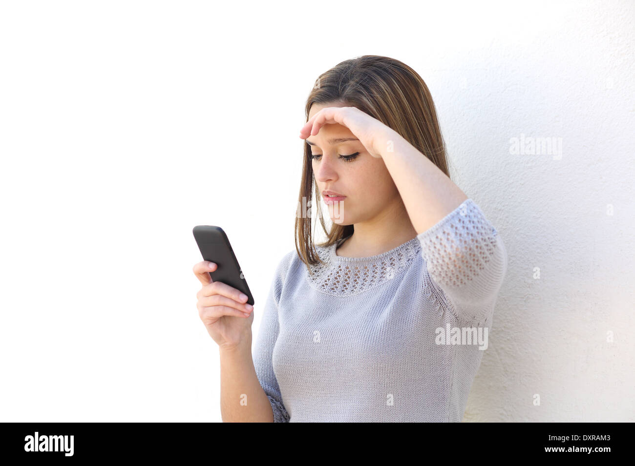 Preoccupato donna guardando il telefono cellulare su un muro bianco isolato Foto Stock