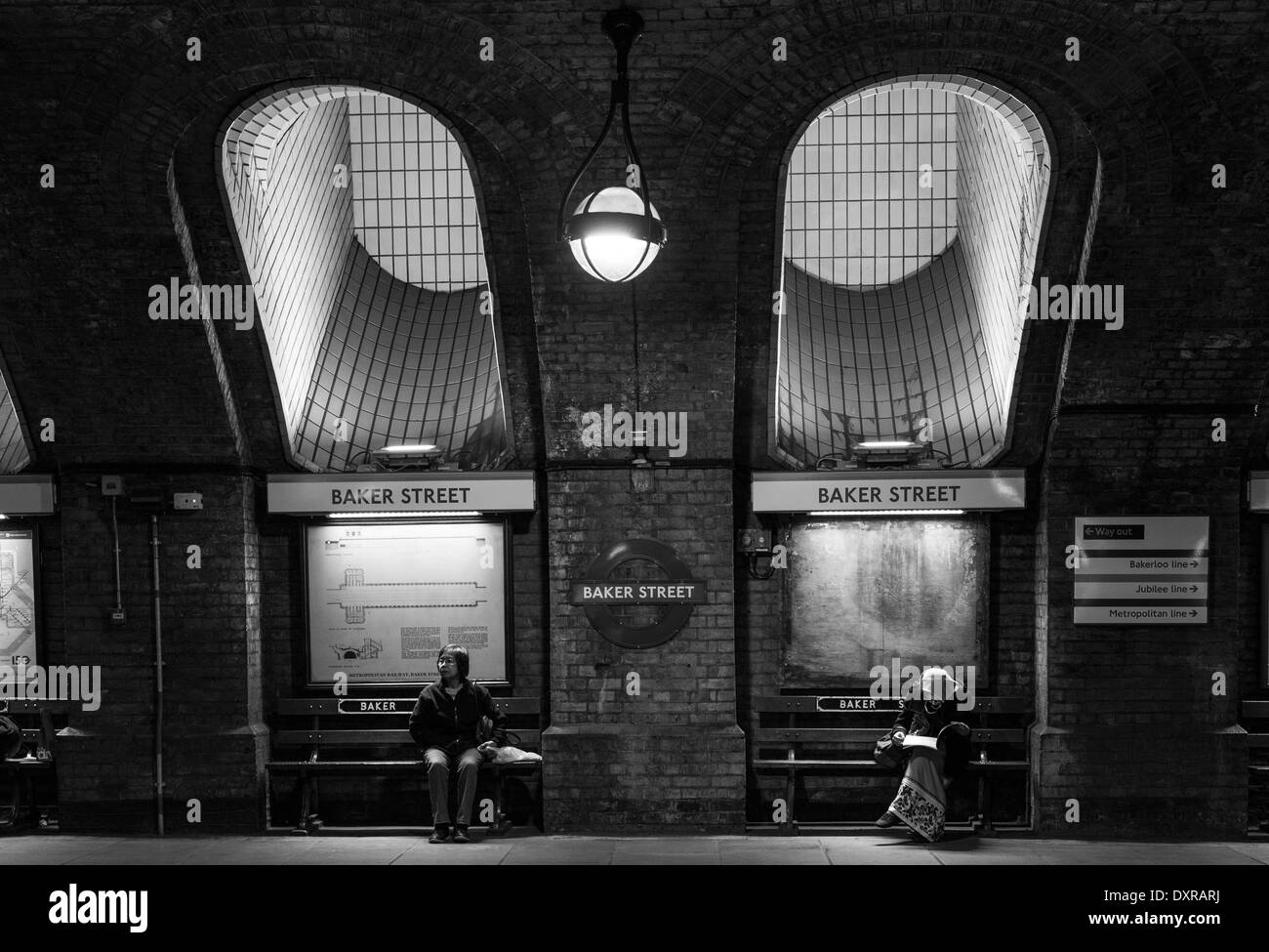 Due persone sedute sui banchi della stazione della metropolitana di Baker street in attesa per il treno. Londra, Regno Unito Foto Stock
