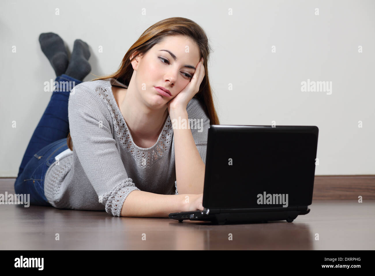 Annoiati ragazza adolescente browsing social media in un notebook sdraiato sul pavimento a casa. Foto Stock