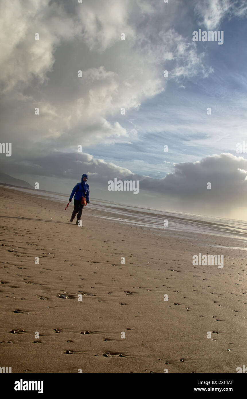 Una donna che cammina su Drigg's Beach su una soleggiata blustery fredda giornata di gennaio. La spiaggia vuota e il vasto cielo dà un senso di spazio Foto Stock