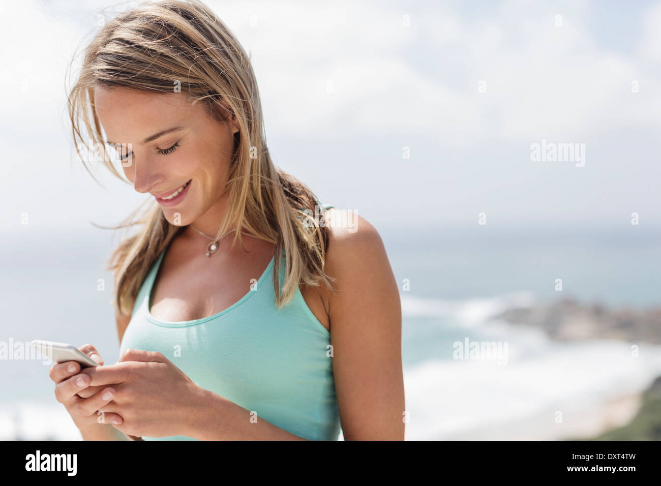 Donna sorridente texting con un telefono cellulare di fronte oceano Foto Stock