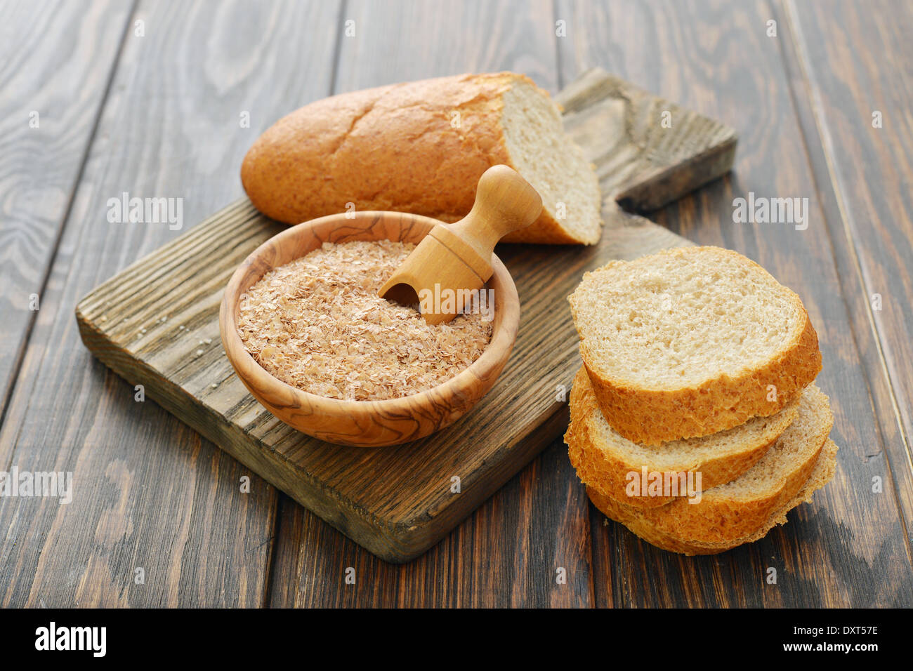 Crusca di frumento nella ciotola con il pane tagliato a fette e su sfondo di legno Foto Stock