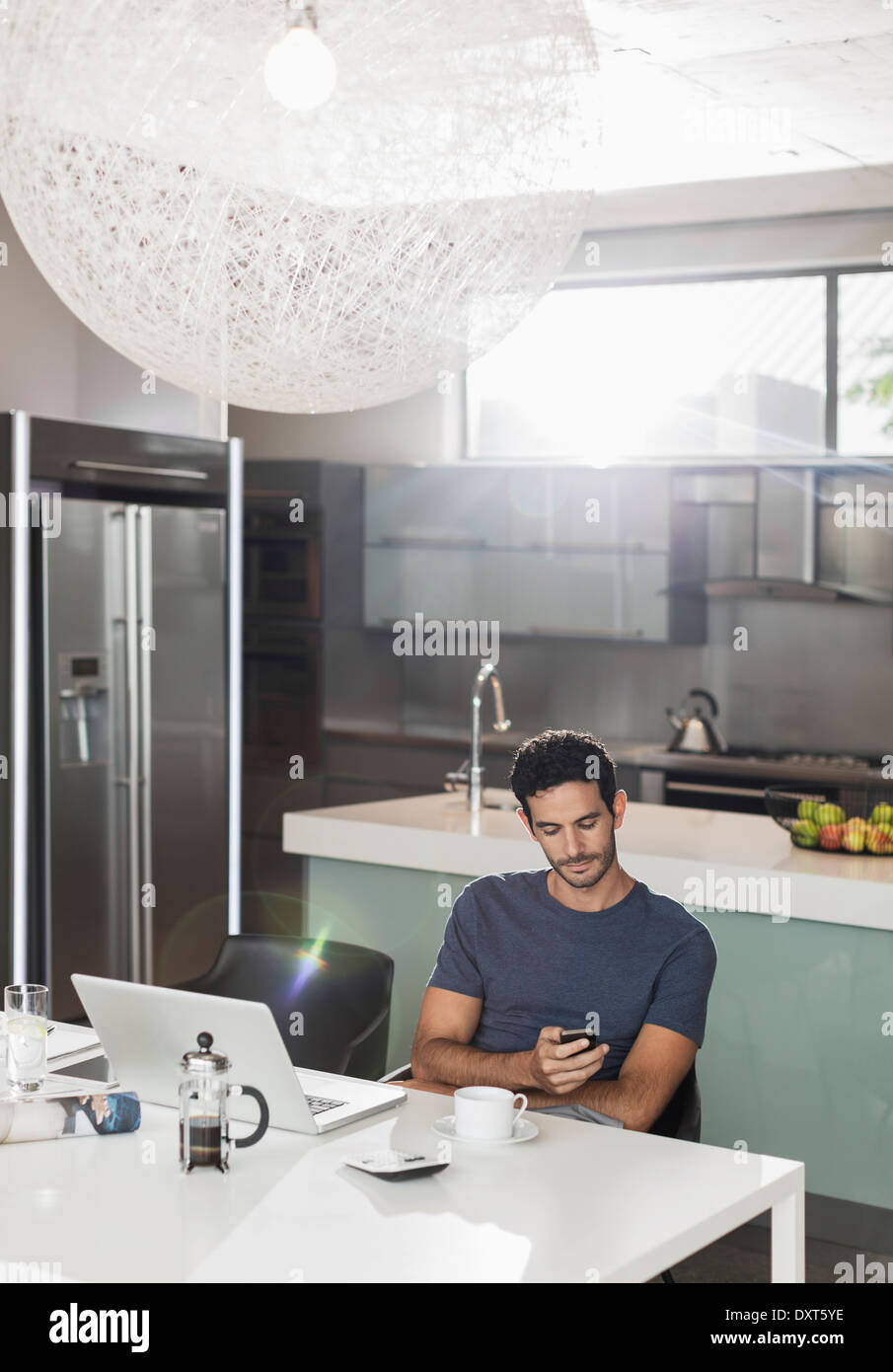 L'uomo texting con un telefono cellulare al tavolo della cucina Foto Stock