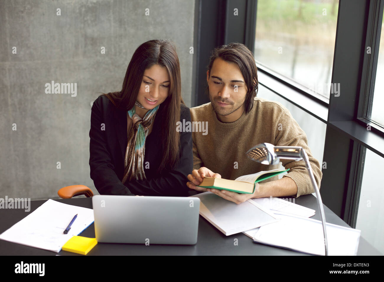 Giovane uomo e donna con laptop e libro in preparazione per gli esami. studenti universitari che lavorano duramente per gli esami finali in biblioteca. Foto Stock