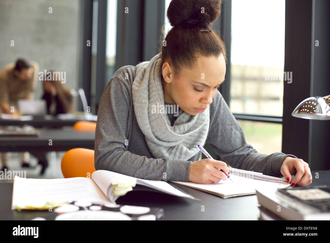 Studentessa prendendo appunti da libri per il suo studio. Giovane americano africano donna seduta al tavolo con i libri per informazioni. Foto Stock