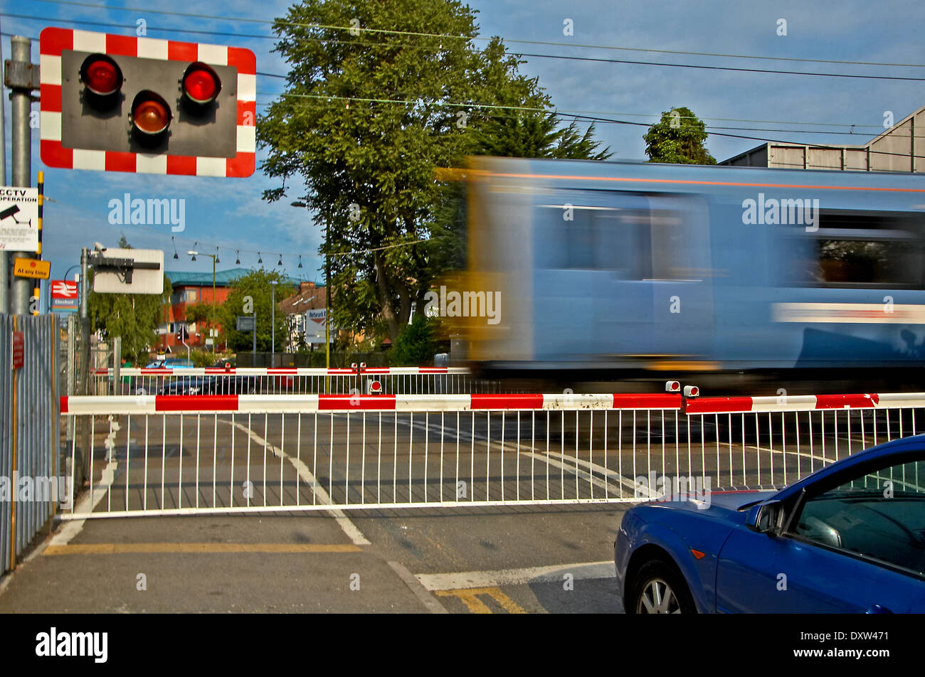 Auto blu in attesa presso un passaggio a livello ferroviario come un blu commuter train velocità passato.. Foto Stock