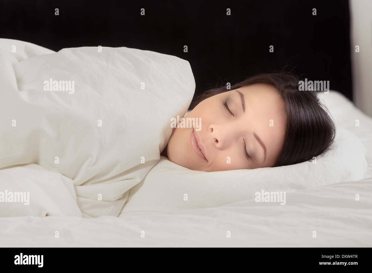Attraente giovane donna godendo un tranquillo sonno nascosto fino a letto a sognare con un espressione serena Foto Stock