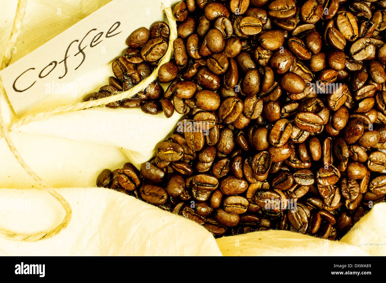 Freschi chicchi di caffè tostati close-up di un tessuto, borsa di tela. L'etichetta con la scritta dalla mano di caffè. Foto Stock