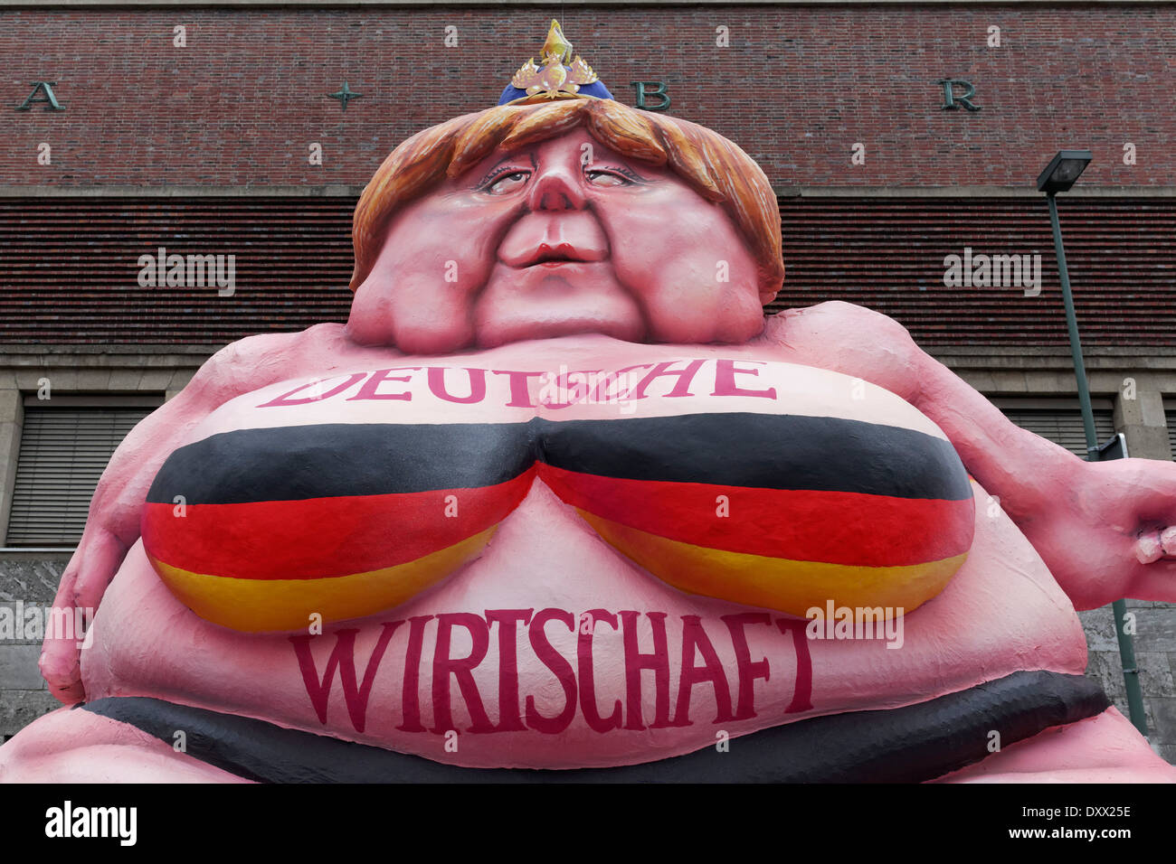 Il cancelliere tedesco Merkel come un grasso Buddha, caricatura politica circa l'economia tedesca, la cartapesta figura per la rosa Foto Stock