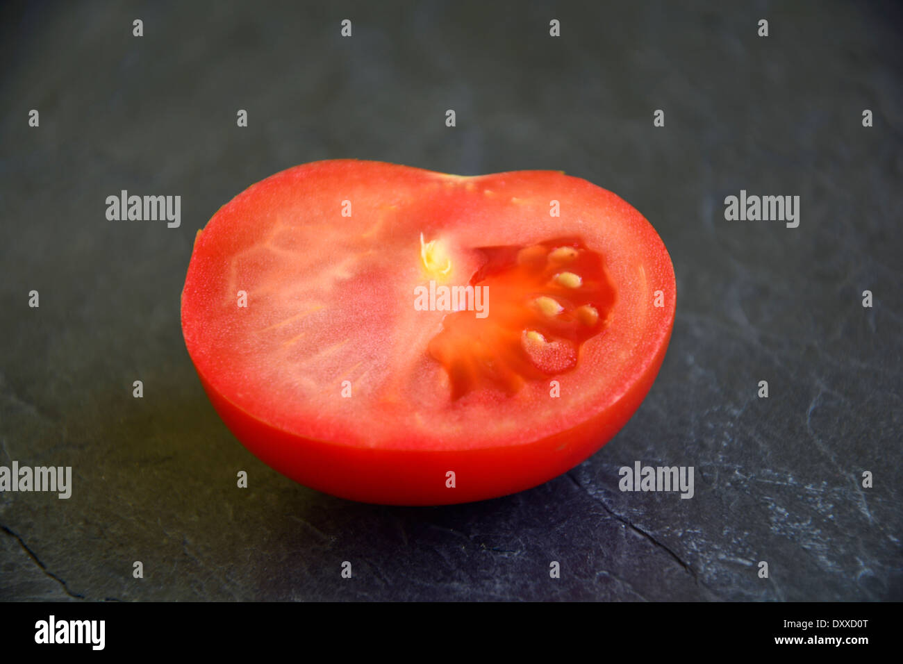 Metà pomodori rossi freschi su un livello di grigio ardesia nera halbierte piastra frische rote Tomate auf grauem schwarzen Schiefer Tomatenhälfte Foto Stock