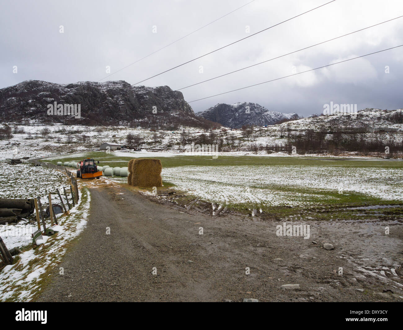 Gjesdal Rogaland Norvegia, tra l'inverno e la primavera, montagne e terreni agricoli, neve sul campo verde, trattore fango e hayball Foto Stock