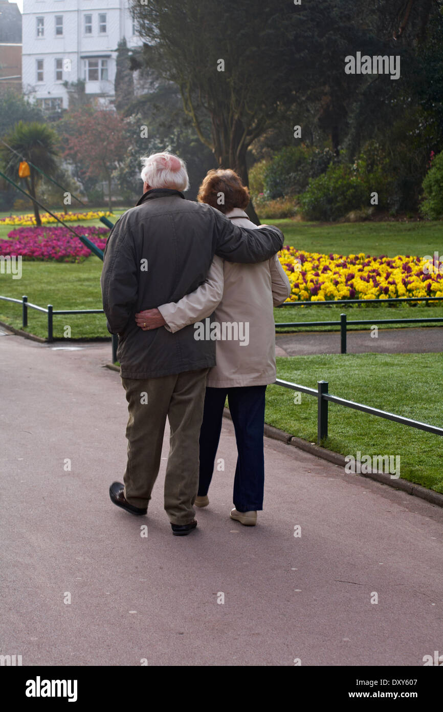 Coppia di anziani camminare a braccetto attraverso giardini di Bournemouth nel mese di aprile Foto Stock