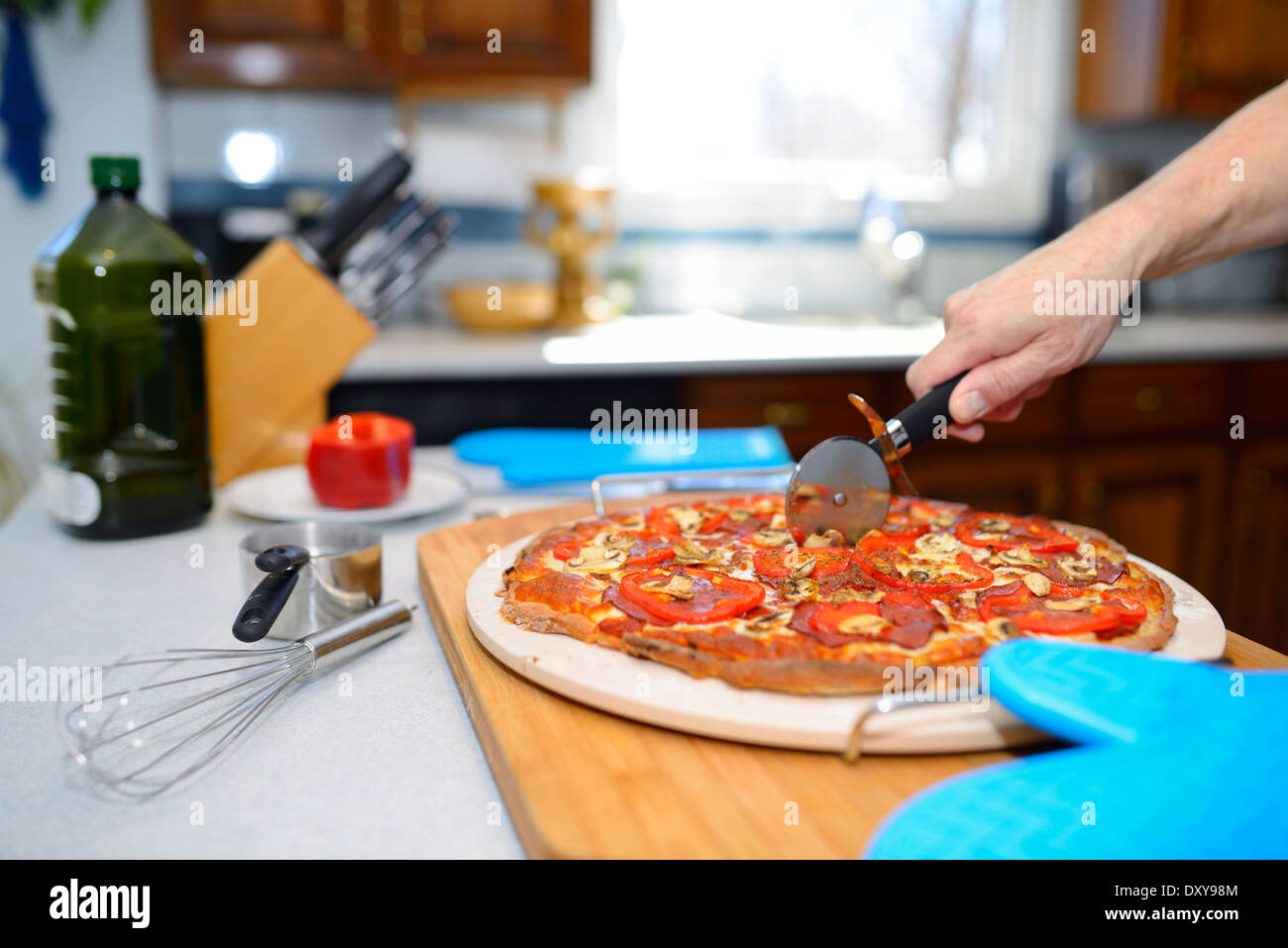 L'uomo il taglio di un caldo senza glutine pizze su una calda pietra di cottura in cucina a casa Foto Stock