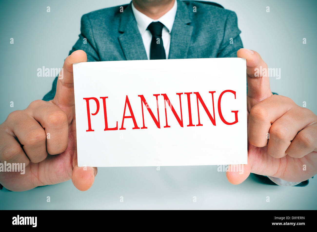 Imprenditore seduti ad una scrivania che mostra un cartello con la pianificazione del testo scritto in esso Foto Stock