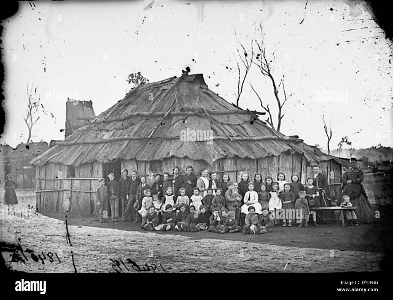 Questa fotografia, scattata tra il 1871 e il 1875, mostra un insegnante con scolari fuori dalla loro scuola a Blacklead (?), Australia. L'edificio, fatto di corteccia, è raffigurato in questa immagine in vetro negativo, che offre informazioni sulla scolarizzazione durante l'era della corsa all'oro. Foto Stock