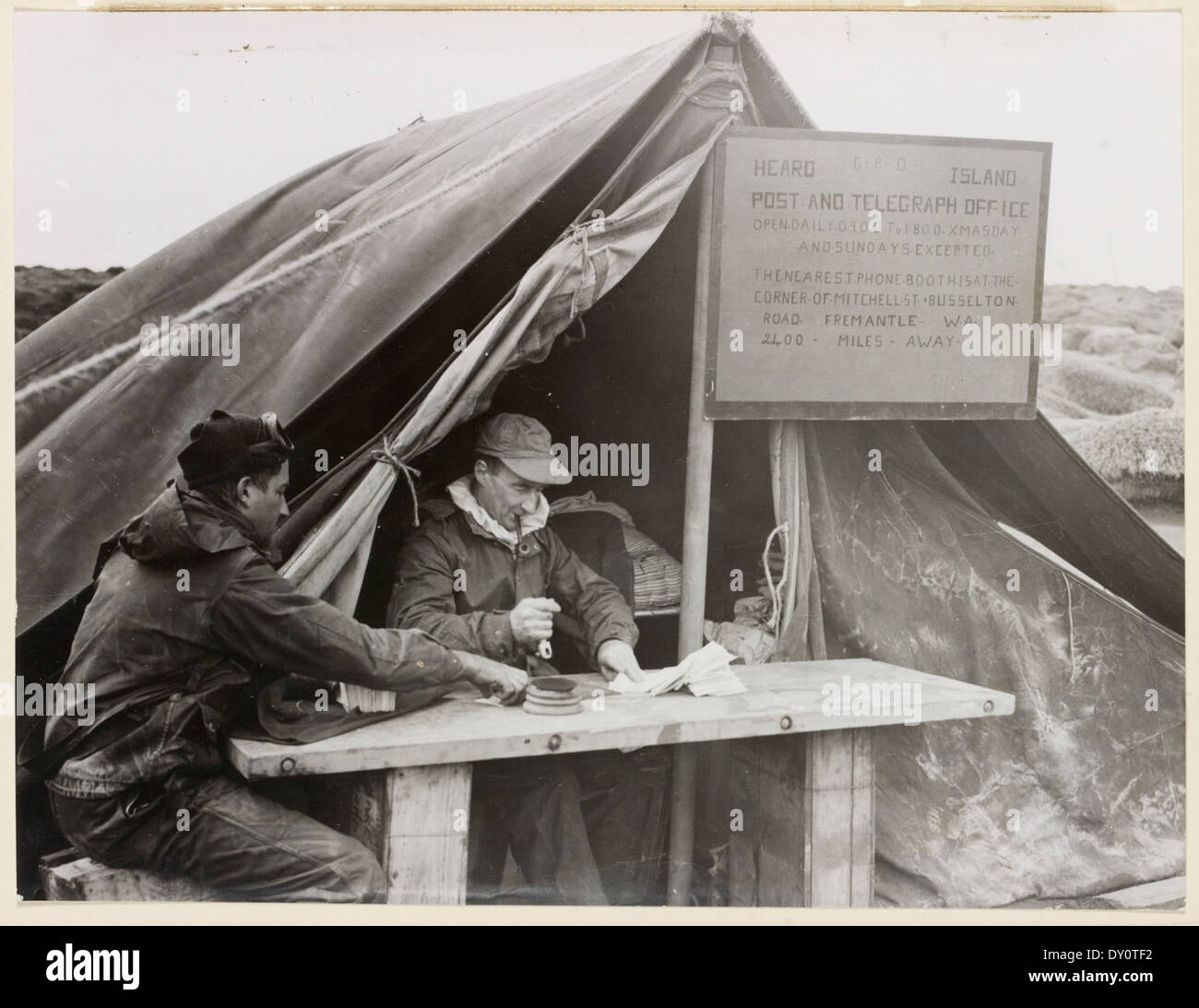 Il Capitano del gruppo S.A. Campbell, insieme all'assistente L. Macey, apre il primo ufficio postale australiano in Antartide durante gli anni '1950 Questo evento importante si è svolto a Heard Island, segnando un importante traguardo nelle operazioni antartiche dell'Australia. Foto Stock