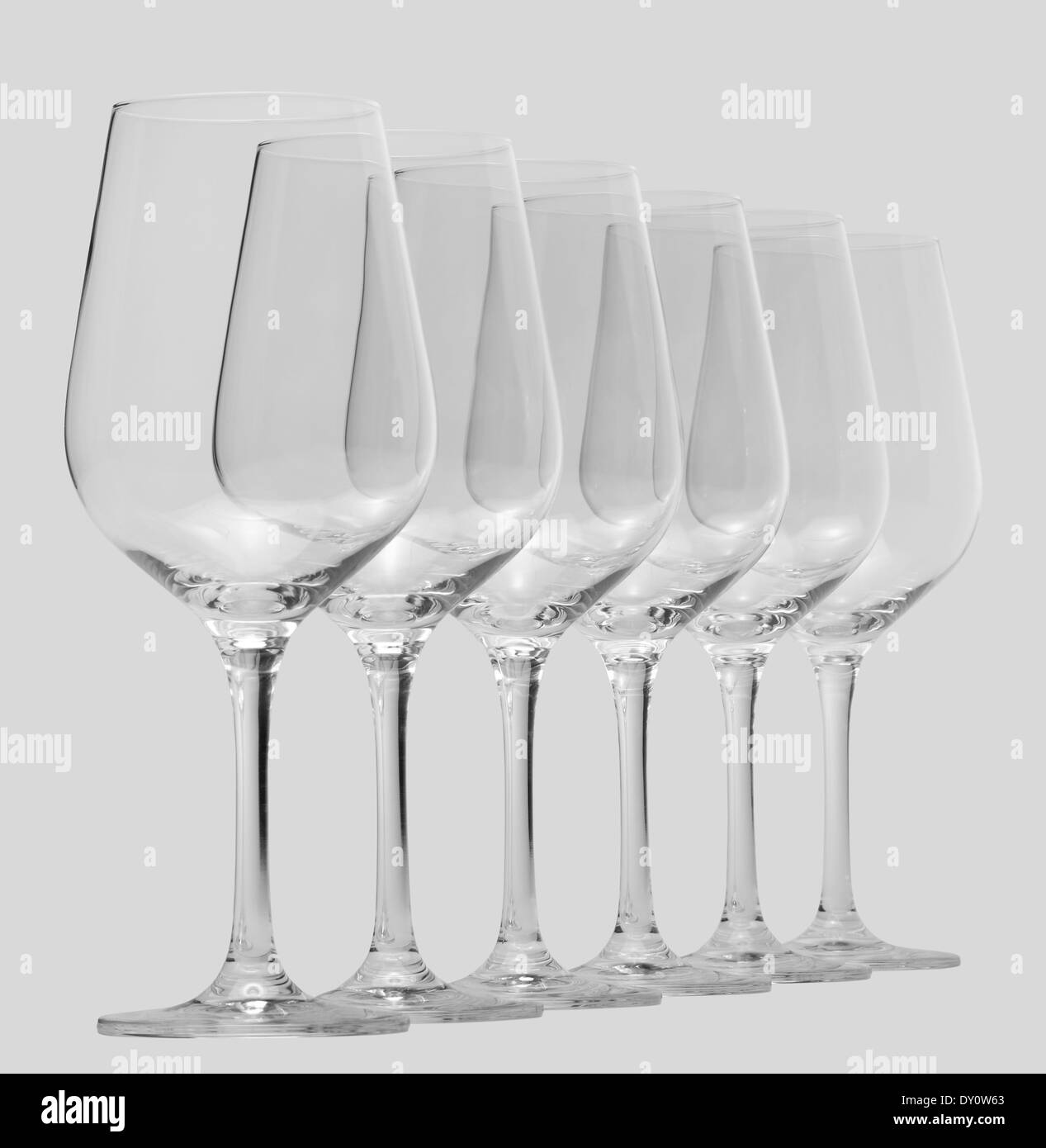Alcuni vuoti e puliti bicchieri di vino in piedi in una fila in grigio chiaro indietro Foto Stock