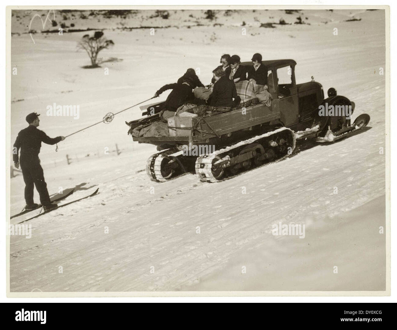 Questa fotografia storica, scattata da Sam Hood, mostra un camion con battistrada caterpillar che tira uno sciatore attraverso la neve a Kosciusko. La scena riflette gli sport invernali e i metodi di trasporto dei primi anni del XX secolo. Foto Stock