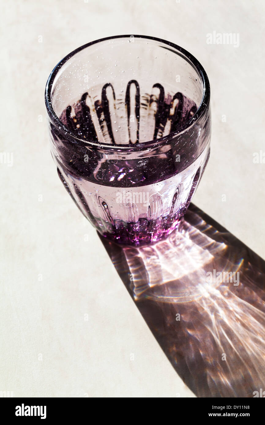 Viola sfaccettata in vetro con acqua chiara illuminata dalla luce del sole Foto Stock