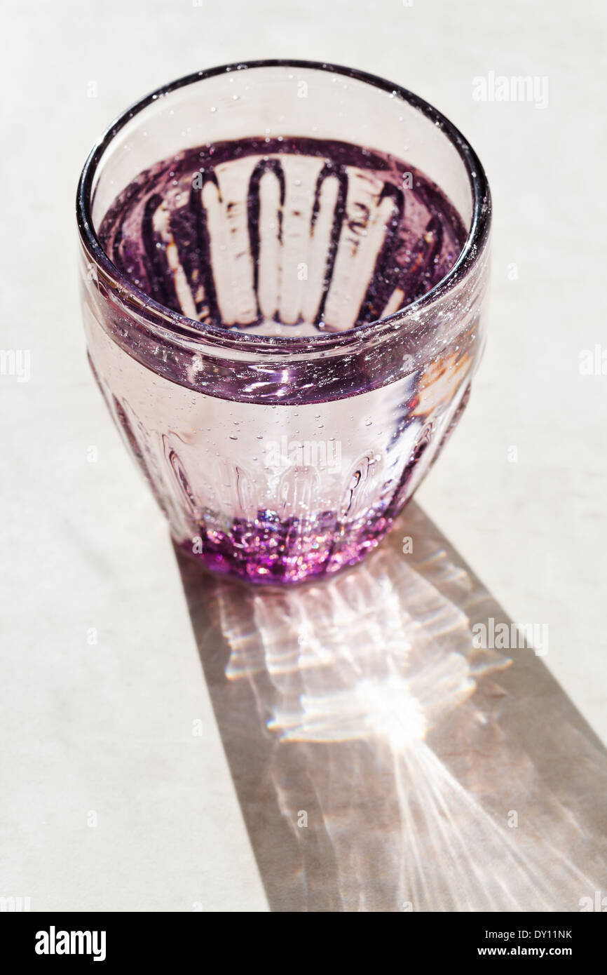 Viola sfaccettata in vetro con acqua sorgiva illuminata dalla luce del sole Foto Stock