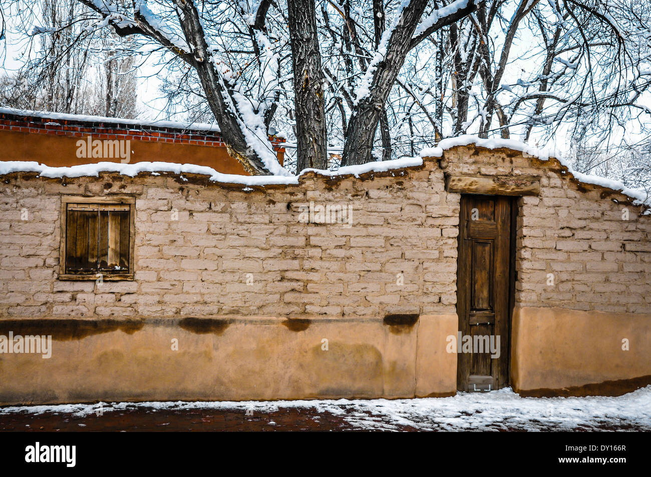 Una scena di neve offre un molto vecchio e affascinante adobe parete e porta in legno che conduce al cortile nella zona storica di Santa Fe, NM Foto Stock