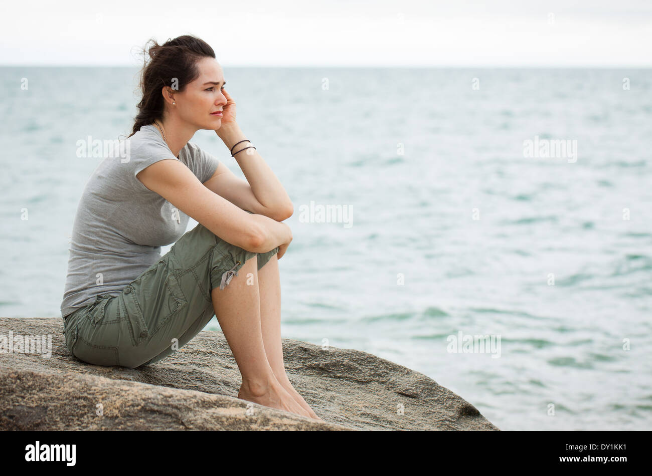 Un triste e depresso donna seduta dall'oceano profondo nel pensiero. Foto Stock