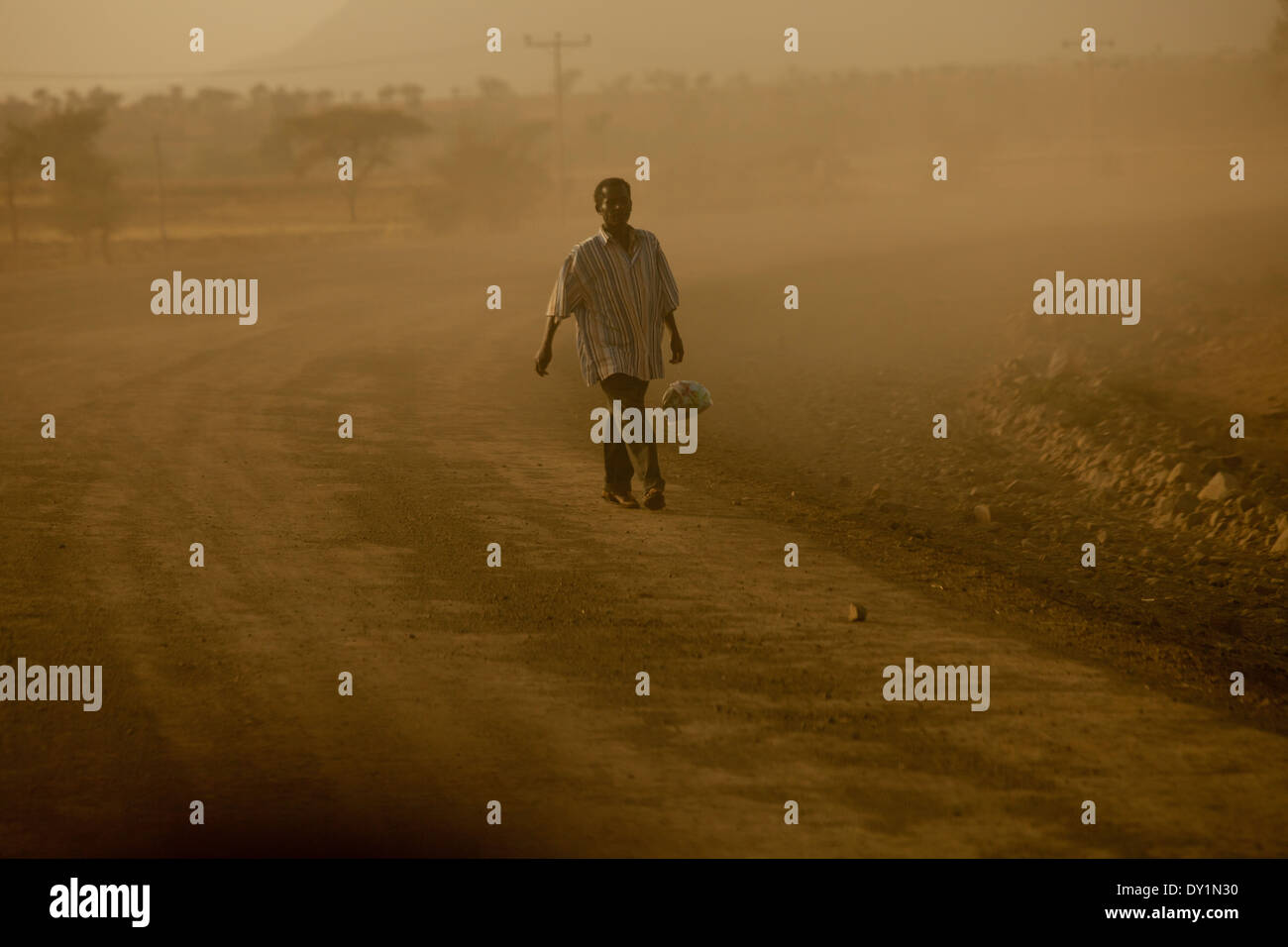 L'uomo africano che porta un sacco camminando sulla strada polverosa Foto Stock