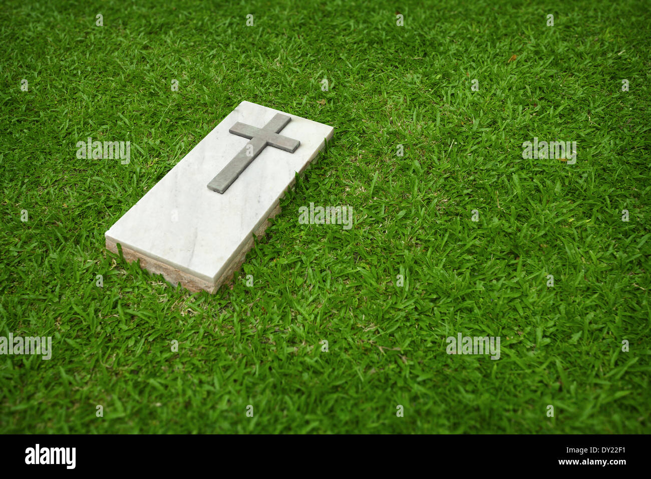 La lapide in marmo con la semplice croce cristiana su di un prato verde Foto Stock