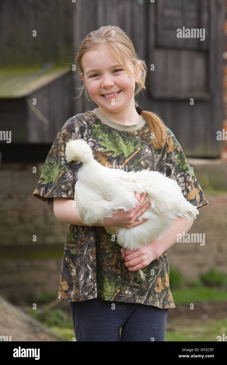 Una giovane ragazza con un bianco di pollo Silkie fuori con un di legno casa della gallina in background Foto Stock