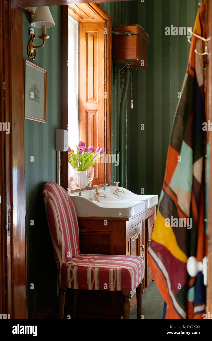 Un ferro di cavallo presidente coperto in Pennant striped biancheria da Oka in bagno con verde scuro Soho carta da parati a strisce da Cole e figlio Foto Stock
