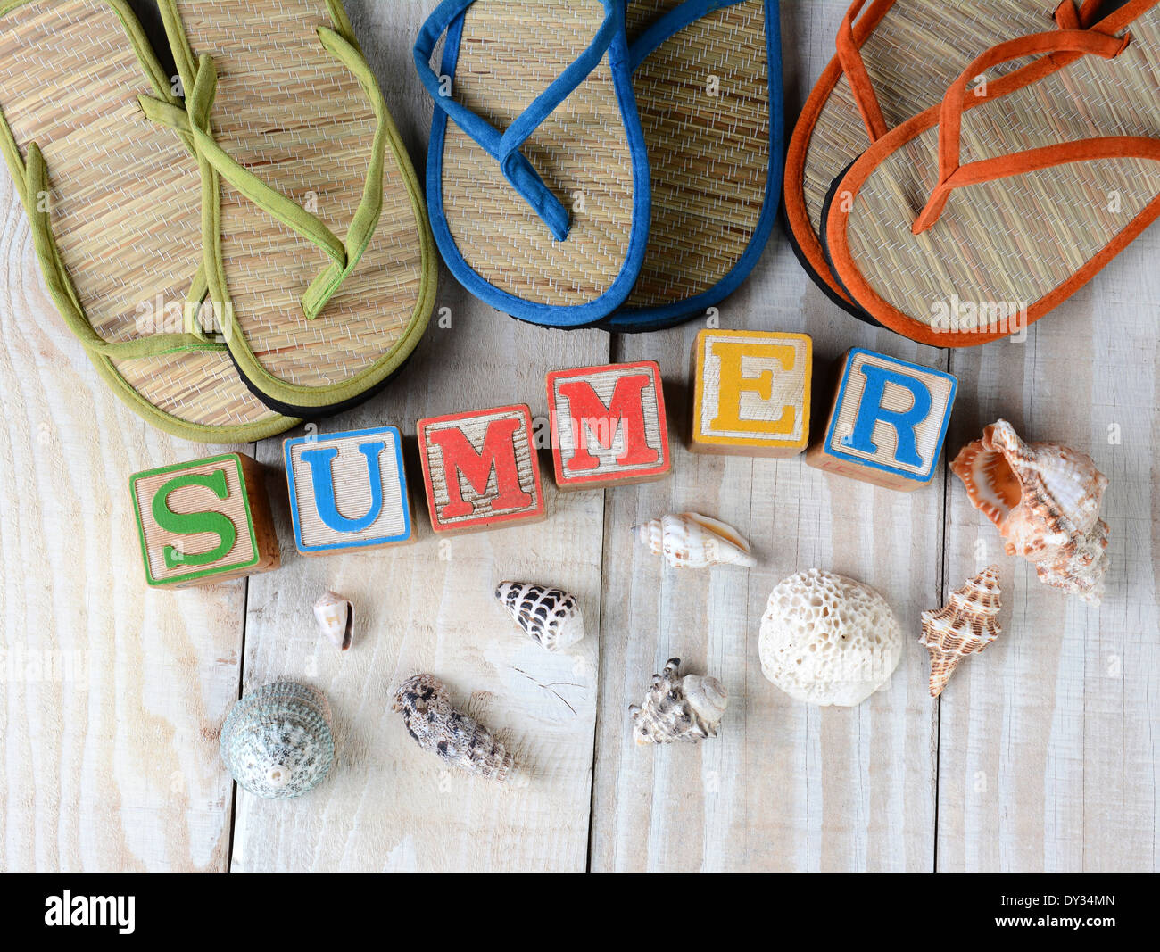 Blocchi per bambini compitazione estate su rustiche tavole in legno la parola è circondata dal mare conchiglie, e flip-flop sandali di stile. Foto Stock