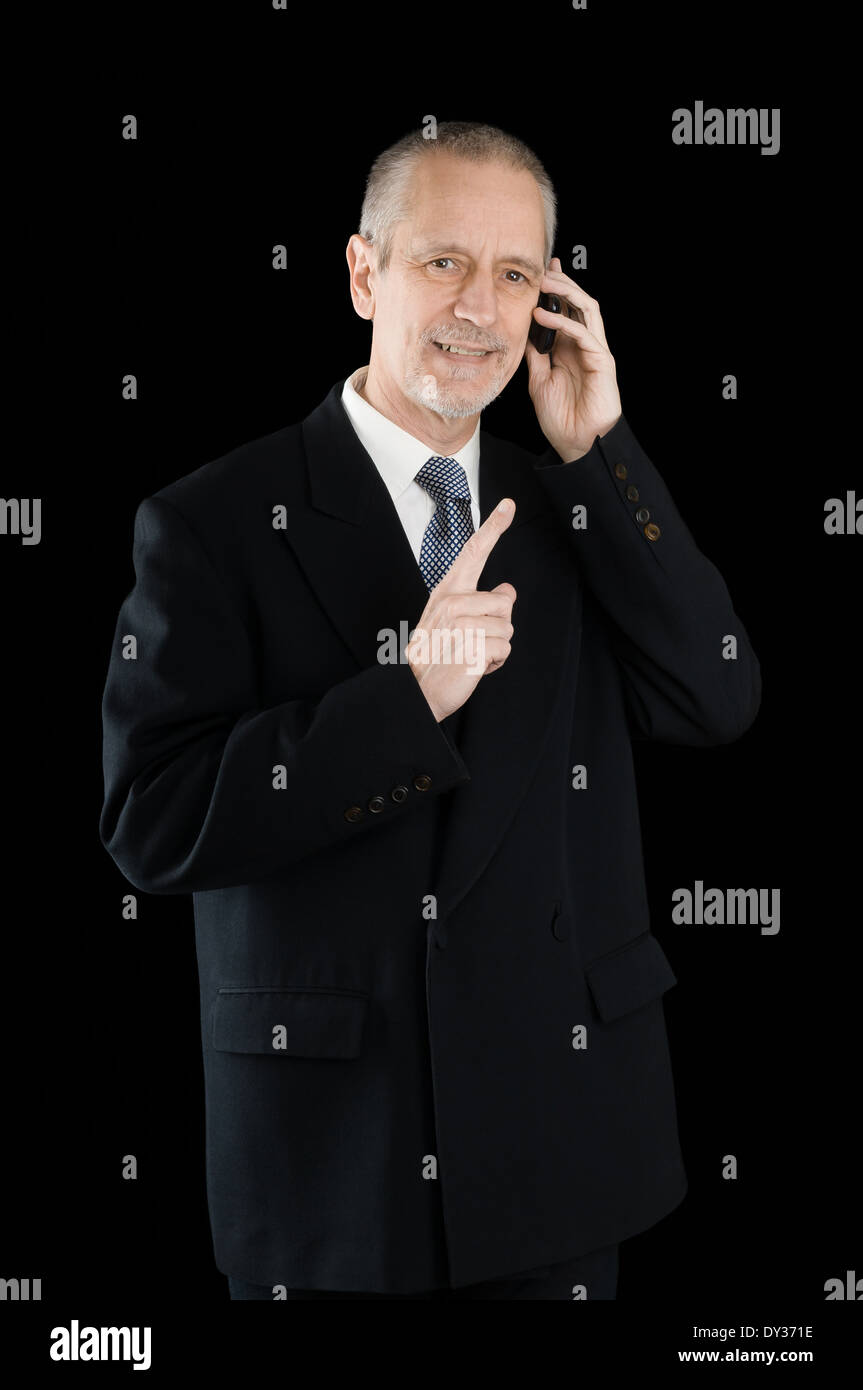 Un gradevole imprenditore indossando un abito nero di sorridere mentre si parla al telefono cellulare, su sfondo nero Foto Stock